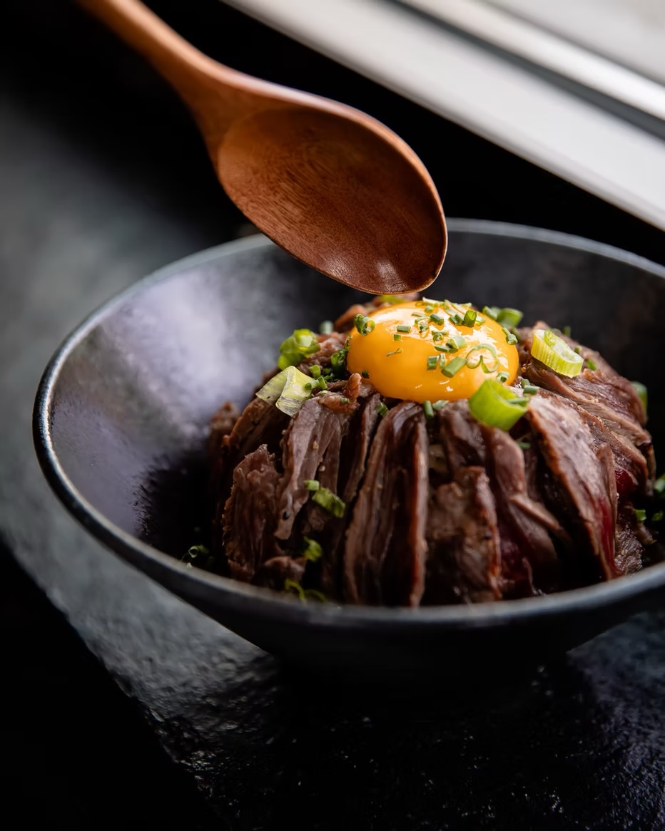 Charred beef over rice crowned with an egg yolk and green onion