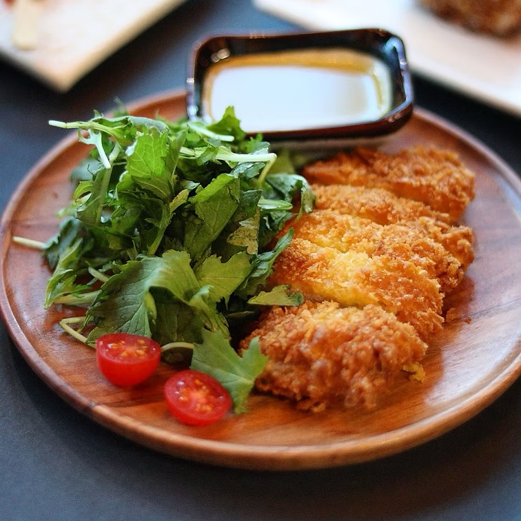 Golden chicken katsu with fresh greens and cherry tomatoes on a wooden plate