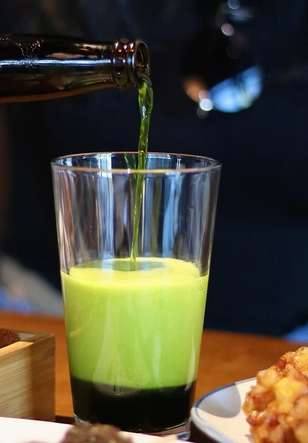 Matcha beer poured bright green into a glass at the table