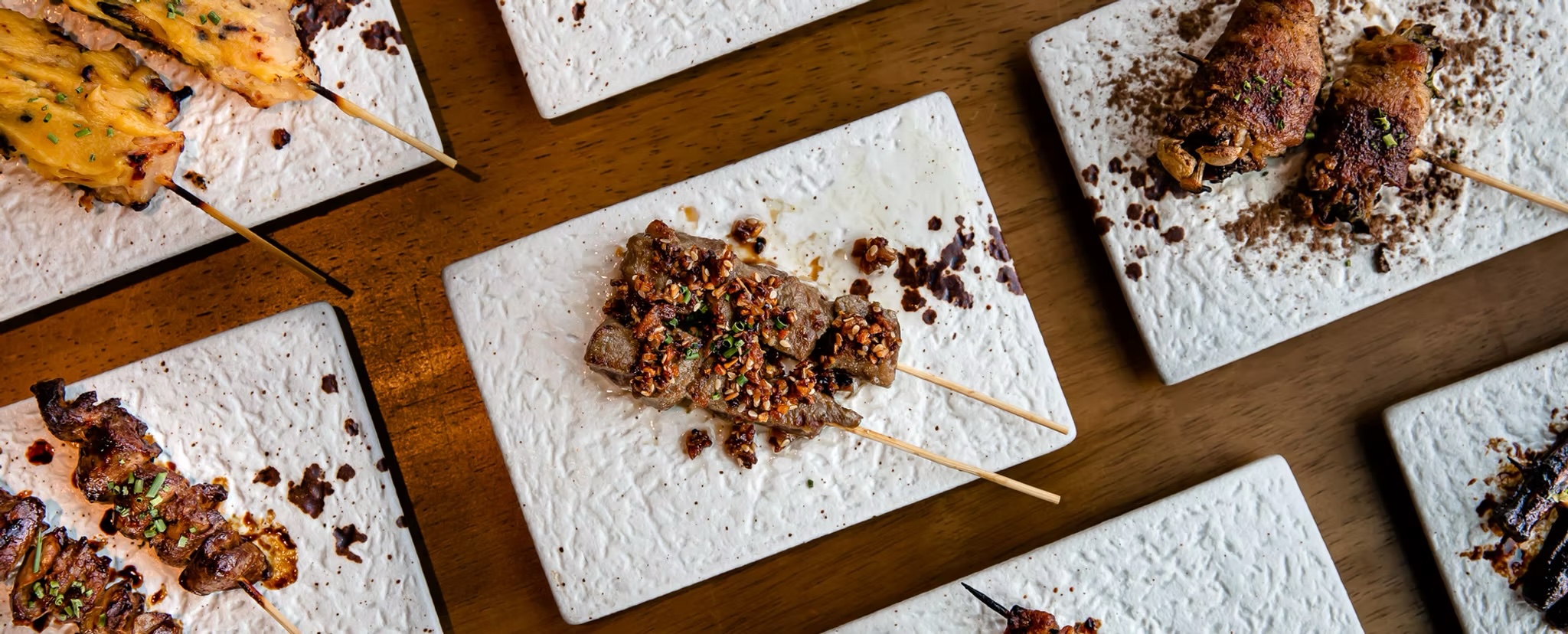 Beef skewers with charred edges laid across white stone plates